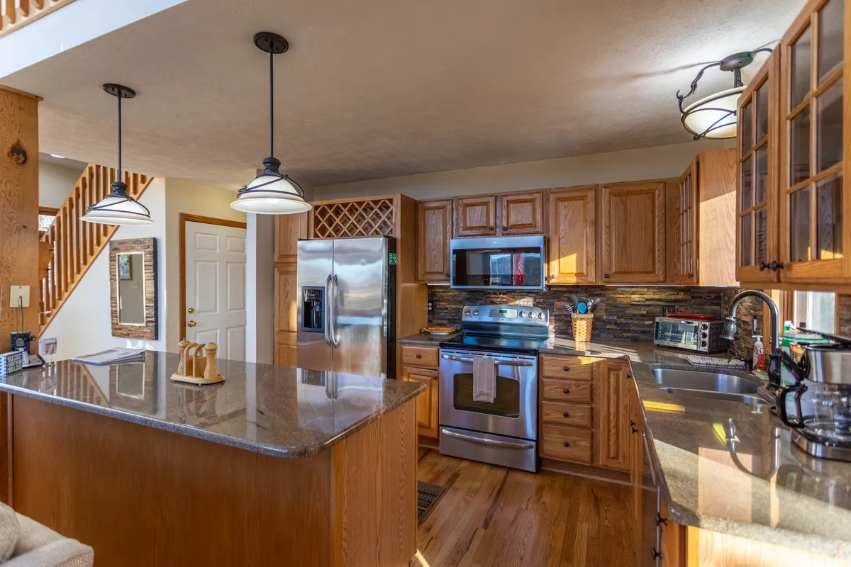 A recently renovated galley kitchen with a central island, stainless steel appliances, granite countertop, and warm wooden cabinetry. The kitchen exudes a welcoming atmosphere, perfect for preparing meals and entertaining family or friends.