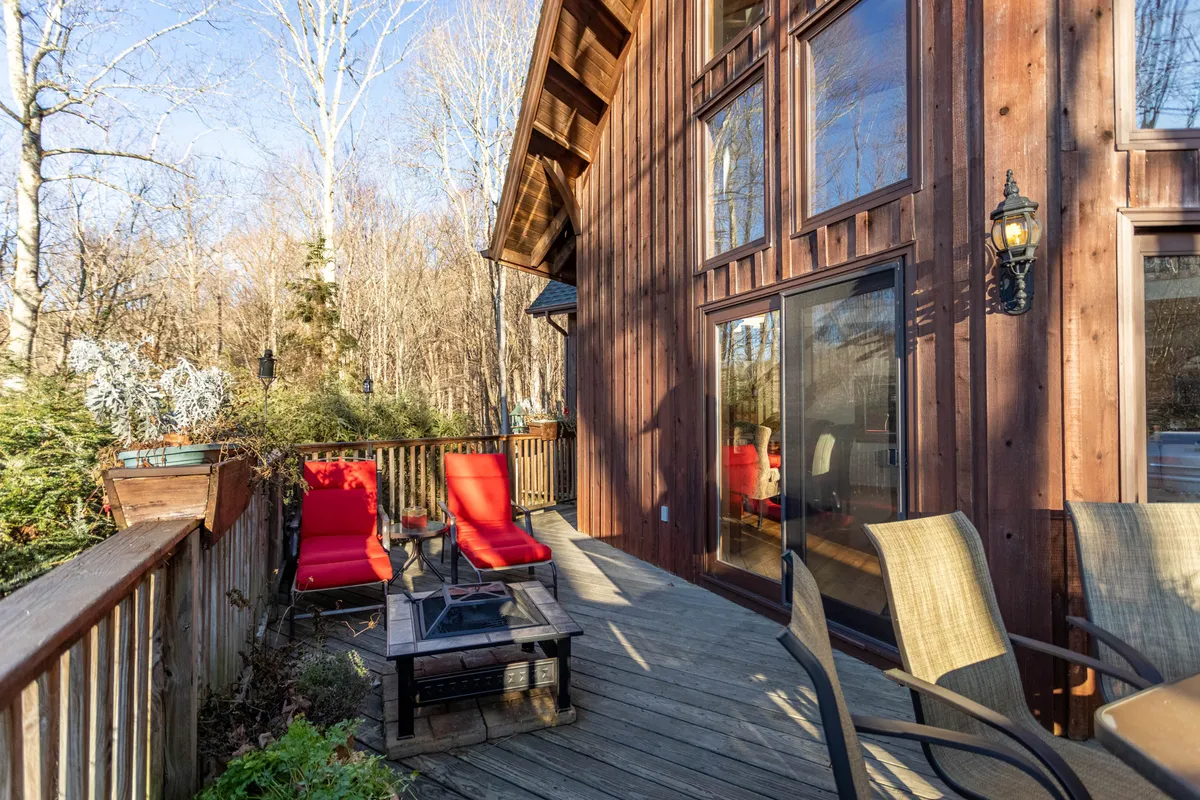 A welcoming wooden deck furnished with red lounge chairs, an outdoor table, and large windows connecting to the interior living spaces. The scene is bright and inviting, with clear evidence of a seamless transition between indoor and outdoor living.