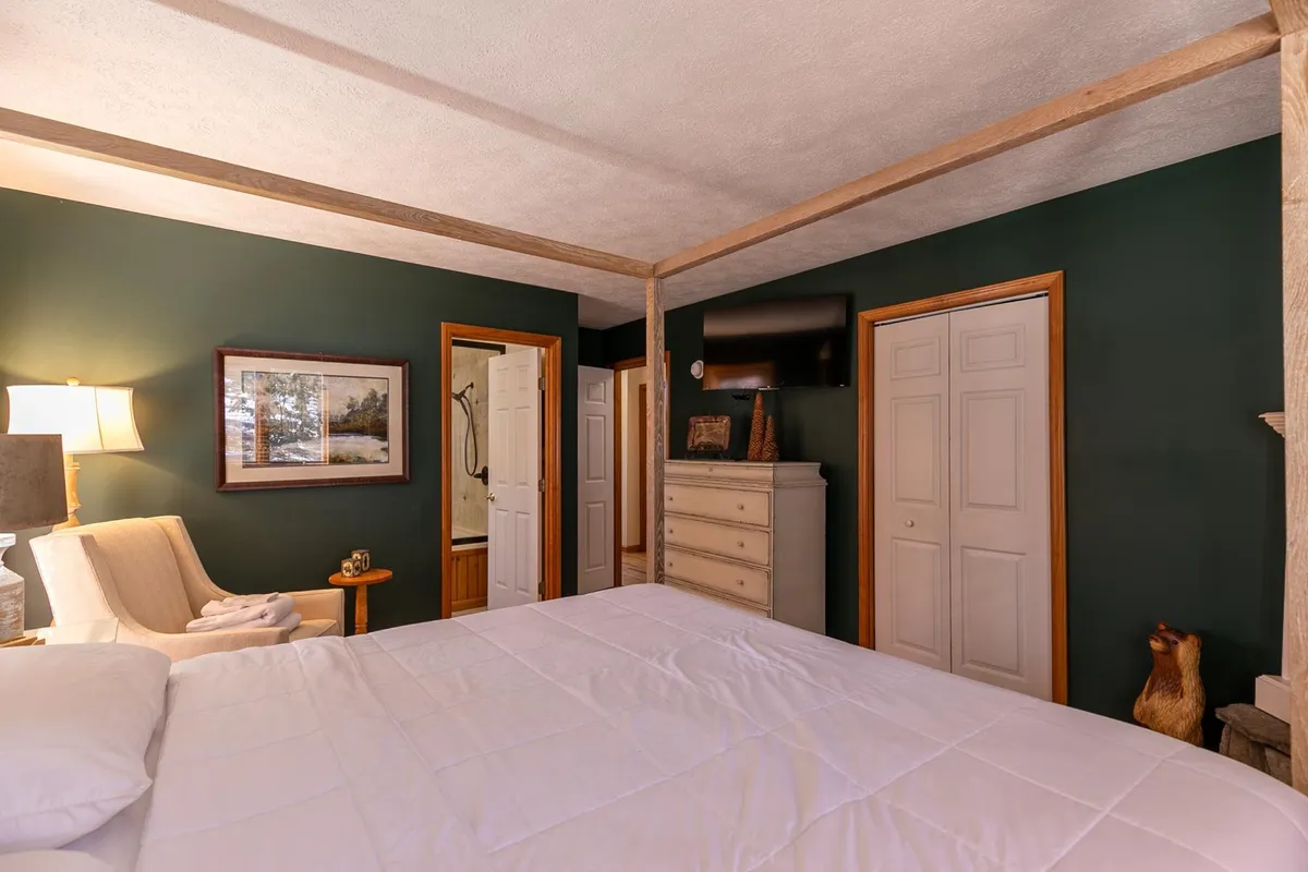 A comfortable bedroom showcasing a four-poster bed with inviting bedding, a classic dresser, wall art, and a nightstand topped with a warm lamp. The ambiance is restful and intimate, making it welcoming for guests of all ages.