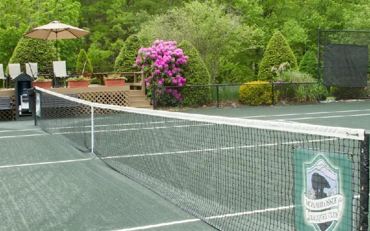 A vibrant tennis court surrounded by flowering bushes and shaded seating areas, inviting both active play and leisurely relaxation. The setting is lively yet peaceful, communicating both the amenities and the resort's welcoming atmosphere.