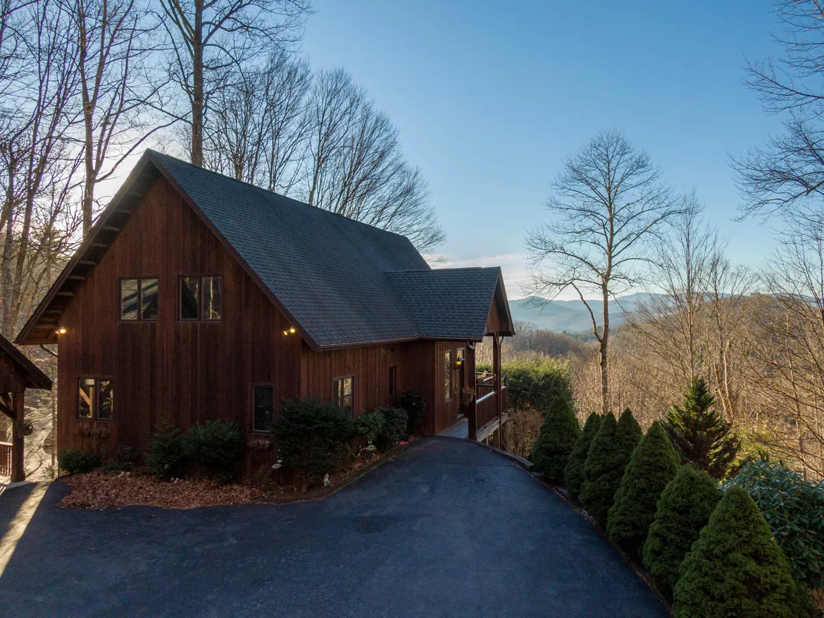 A wooden home nestled among trees, with a spacious deck overlooking distant mountains. The inviting porch and natural surroundings hint at family gatherings, peaceful mornings, and outdoor living in a secluded resort setting.