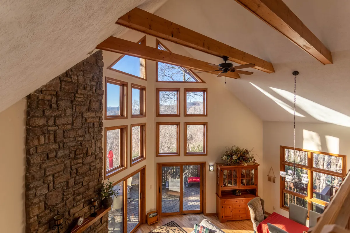A cozy living space with large windows offering sunrise views, a rustic stone fireplace, wooden beams, and inviting furniture. The setting is warm and intimate, ideal for lounging after a day out or sharing quiet evenings fireside.
