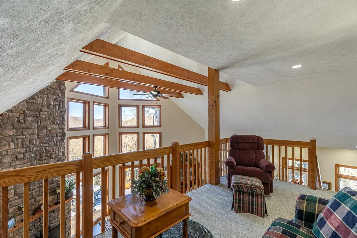 A tranquil seating area with large windows framed by wooden beams, offering an inviting spot to relax and take in panoramic views of the outdoors. The soft, natural lighting and comfortable furnishings evoke a sense of peace and quiet ideal for a couple's getaway.