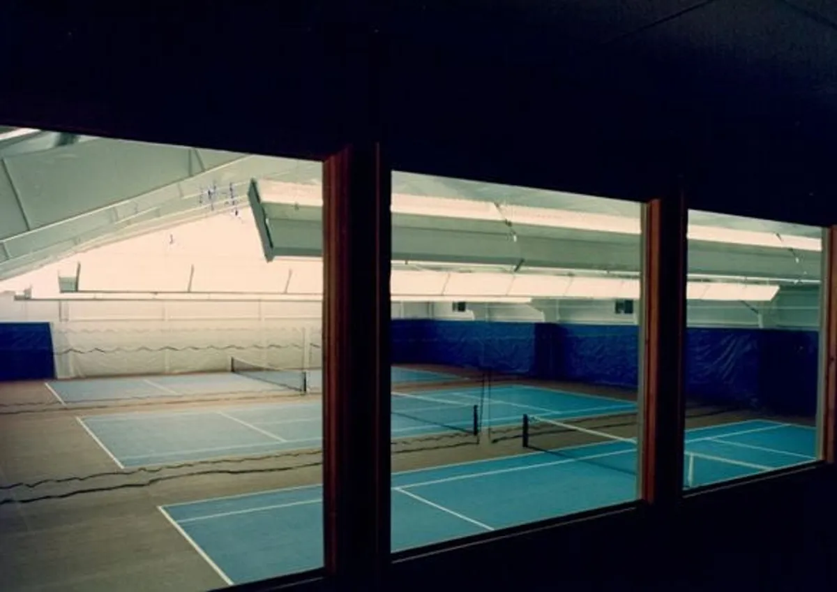 An interior view of polished tennis courts with netting and wooden floors, inviting both casual play and competitive matches. The space feels bright and energetic, designed for community and athletic engagement.