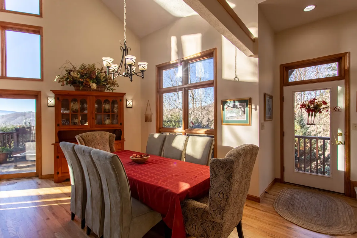 A cozy dining room featuring a large table set beneath a classic chandelier, with cabinets and windows providing a warm, inviting setting. The space invites large groups to gather for meals, celebrations, or simply to enjoy each other's company.
