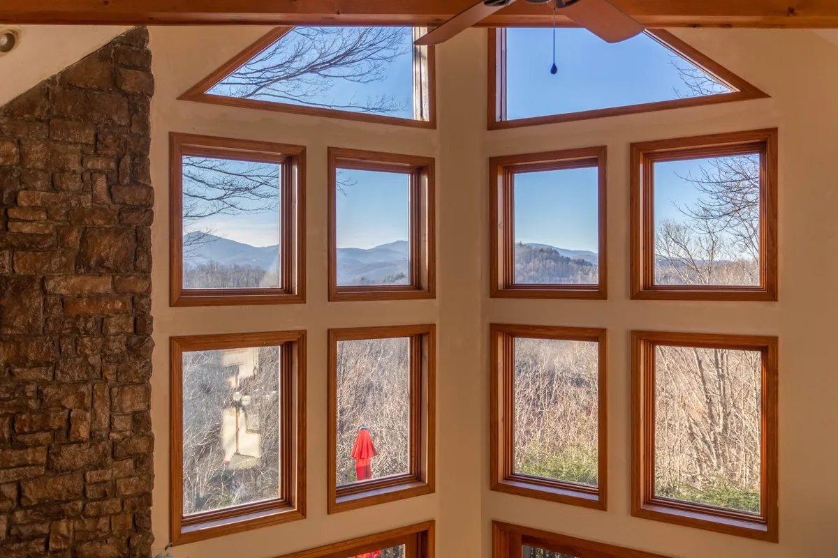This image showcases a tranquil interior space featuring large windows with expansive mountain views, a stone wall, and a cozy, comfortable seating area. The view through the windows suggests a serene, wooded environment with the peaks of distant mountains visible—a perfect visual connection to the retreat's promise of mountain serenity.