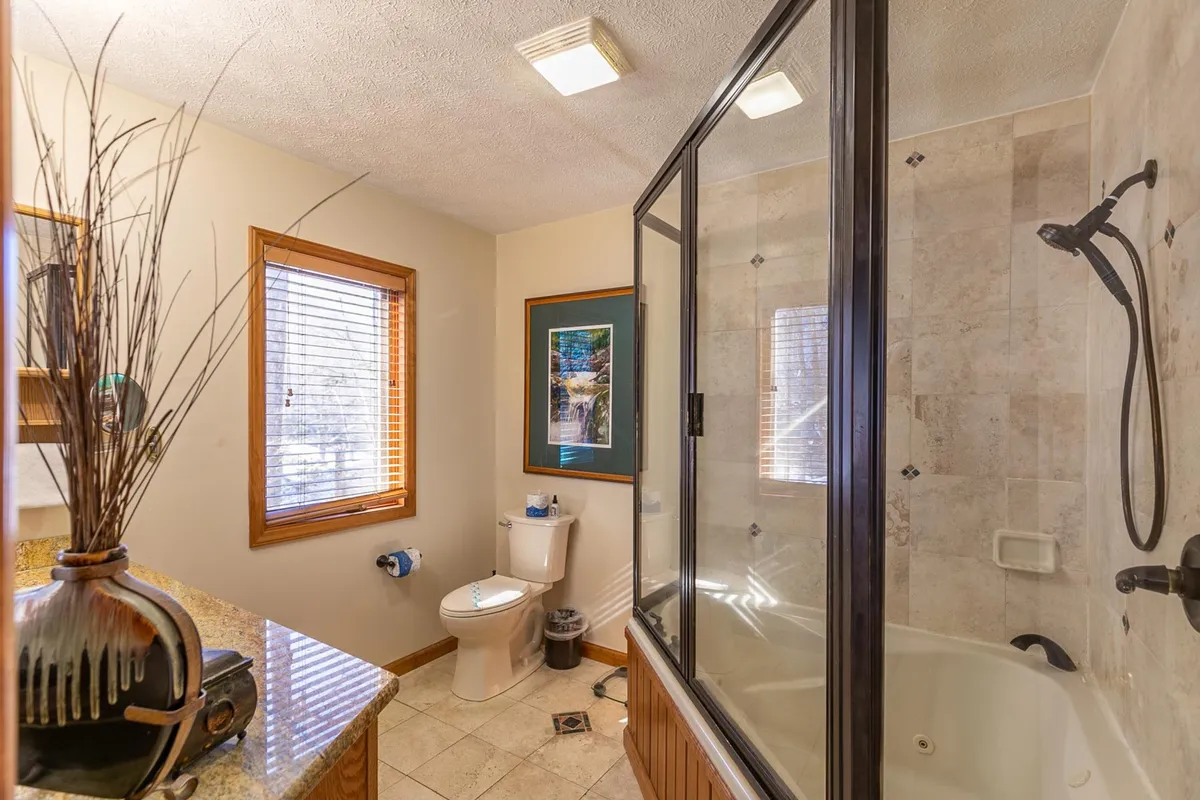 A serene bathroom with a deep soaking bathtub, glass-enclosed shower, and stylish sink area adorned with a decorative vase and framed artwork. Soft natural light filters into the space, highlighting the tranquil and rejuvenating ambiance ideal for relaxation.